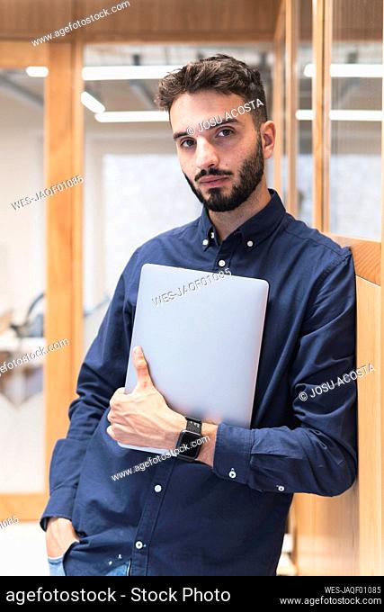 Young businessman with laptop leaning in office