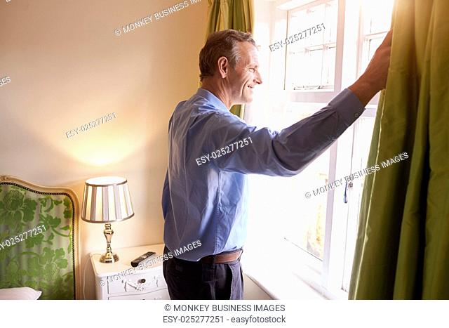 Senior man opens curtains to look at the view from a window
