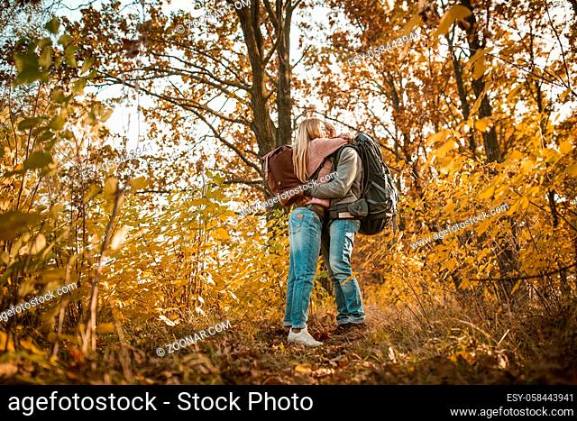 Loving couple of travelers hugs admiring the autumn nature. Young people stand embracing amid multicolor autumn nature. Shot from below