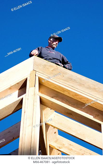 Carpenter standing on the peak of a framed in roof, looking down the rafters at a construction site