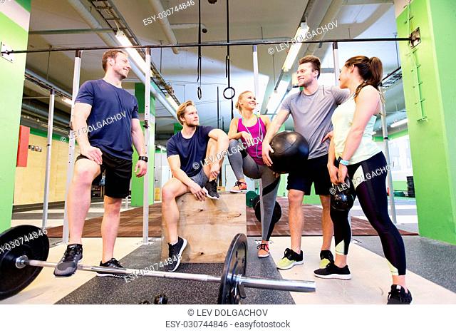 fitness, sport and healthy lifestyle concept - group of happy people with different sports equipment talking in gym