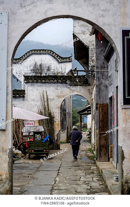 Woman walking in narrow lane, Ancient Chengkan Village, founded during the Three Kingdoms period and arranged on fengshui principles of the unification of yin...