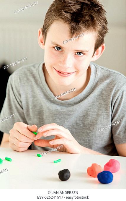 Single smiling boy in gray short sleeve shirt forming small bits of clay from larger pieces on white table