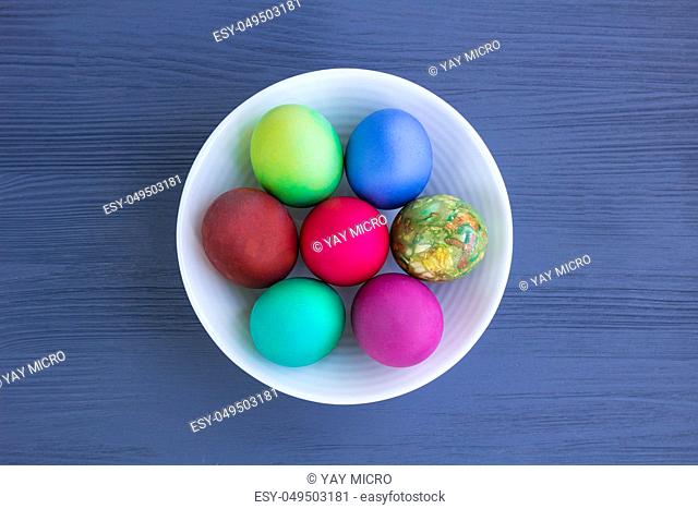 White plate of Easter multicolored boiled eggs decoration on grey wooden background