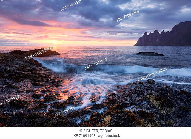 Impressive sunset above the Okshornan cliffs on Ersfjordr in northern Norway, approaching waves in the foreground, Island of Senja, Troms Fylke, Norway