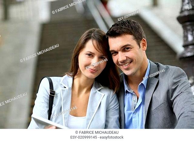Cheerful couple sitting in stairs with electronic tablet