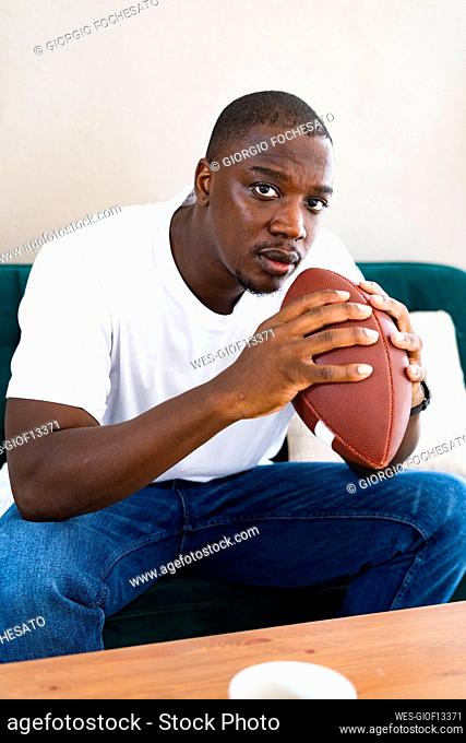 Man holding rugby ball while sitting on sofa at home