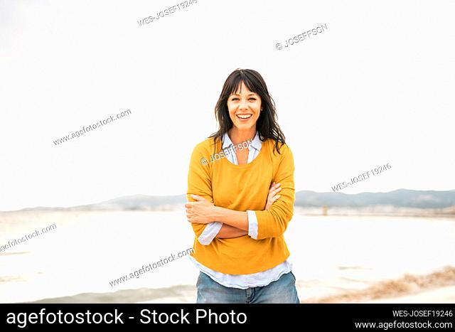 Happy woman with arms crossed at beach