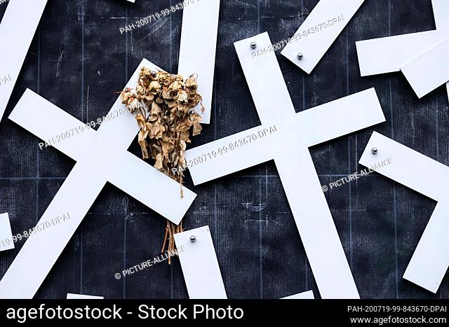 16 July 2020, North Rhine-Westphalia, Duisburg: Withered roses are stuck on a cross at the memorial for the victims of the Love Parade catastrophe