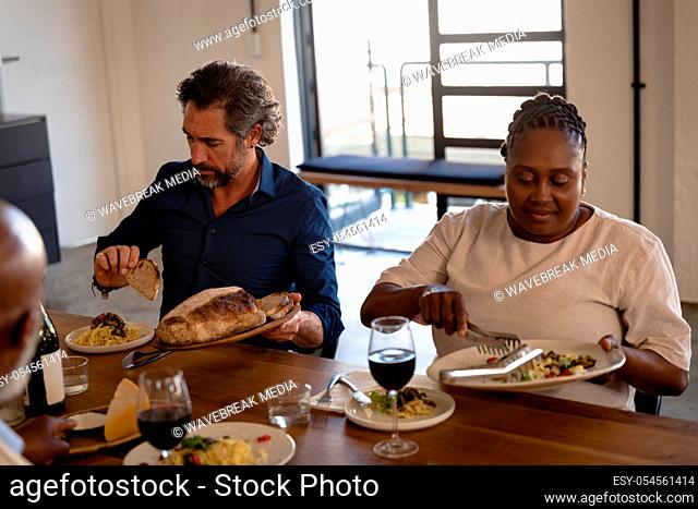 Front view of a Senior Caucasian man and an African woman at cookery class, putting on fresh pasta dish, and bread on their plates, drinking wine