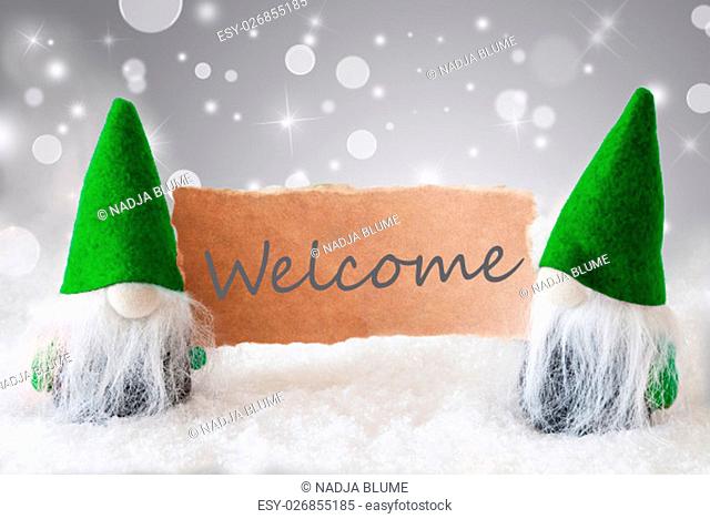 Christmas Greeting Card With Two Green Gnomes. Sparkling Bokeh And Noble Silver Background With Snow. English Text Welcome