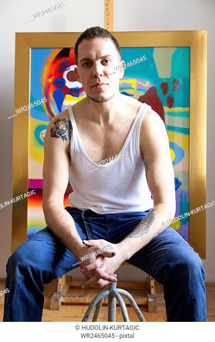 Male painter sitting in art studio with hands clasped