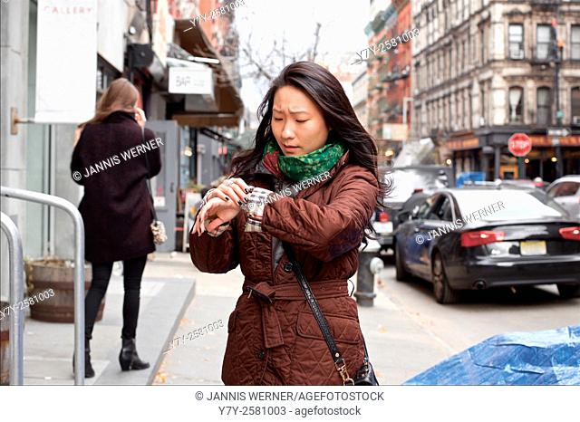 Young Asian woman urgently checks her watch in the streets of Manhattan, New York, NY, USA