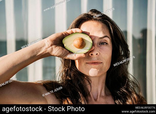 Woman covering eye with halved avocado