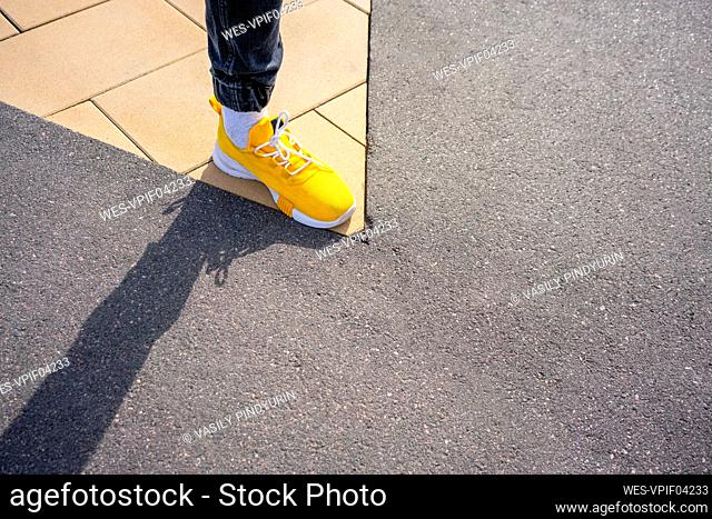 Boy wearing yellow shoe while standing on footpath