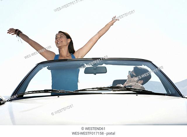Spain, Majorca, Young man driving and woman standing in cabriolet car