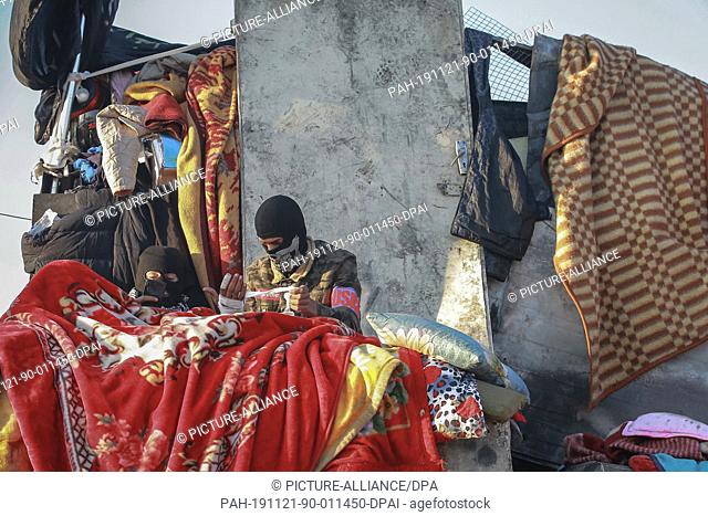 21 November 2019, Iraq, Baghdad: Two masked protesters sit under blankets on the Sinak Bridge across the Tigris river and nearby Tahrir Square amid ongoing...