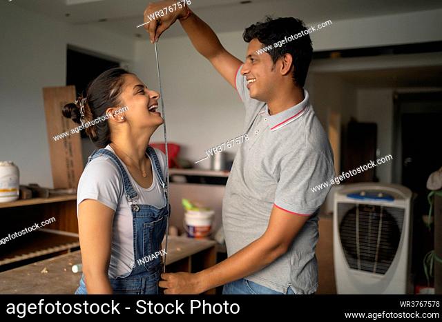 Young newlyweds having fun as the husband places measuring tape against his awife