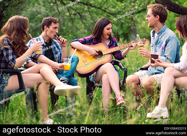 Young people spending quality time together in nature. Friends sitting on chairs out in nature singing some songs with guitar