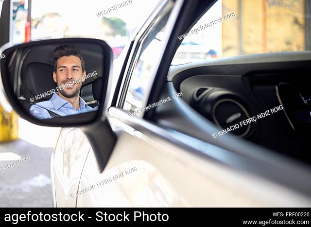 Wing mirror reflection of businessman smiling while driving car