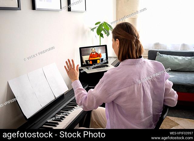 Mid adult woman learning piano with online tutorial on laptop at home