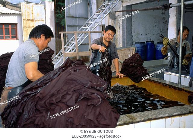 Weishan. Batik factory with men dipping cloths in vats of dye