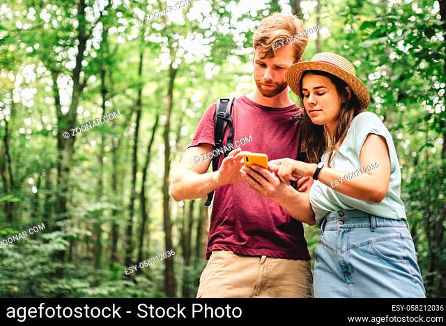 Young caucasian couple uses a smartphone to navigate in the forest. Hiking tourists orientation on the terrain using an online map