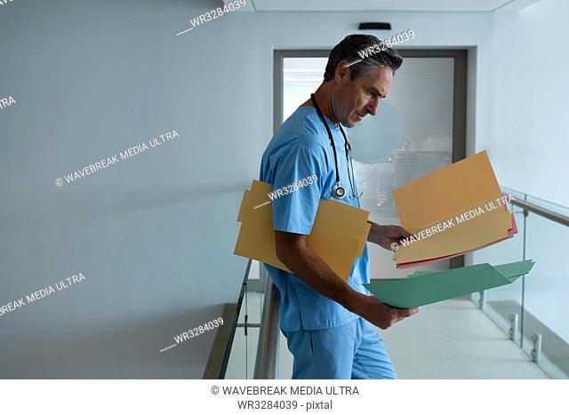 Side view of handsome mature Caucasian male doctor with stethoscope around neck looking at report in corridor in hospital