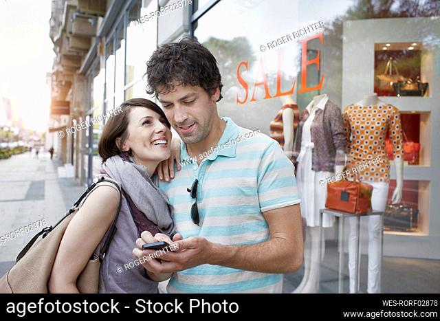 Woman looking at boyfriend using smart phone on footpath