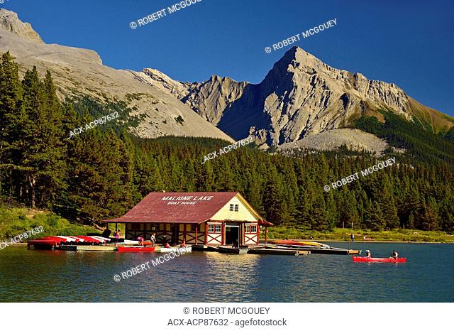 An image of Maligne Lake showing the boat house with people paddeling canoes in the rocky mountains in Jasper National Park Alberta Canada