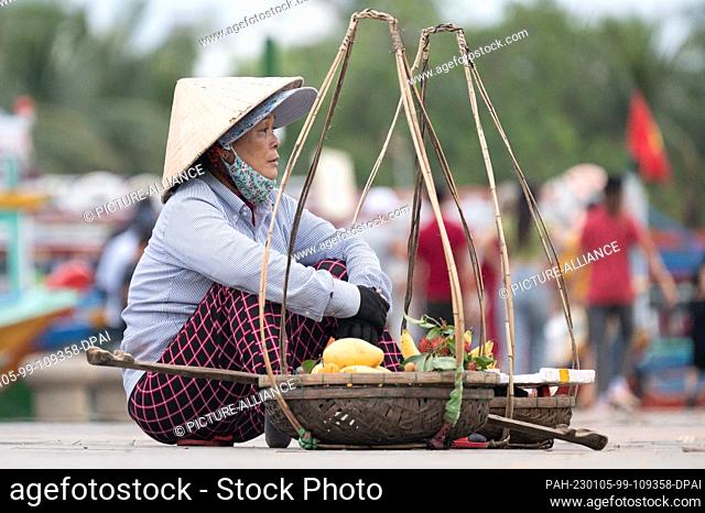 22 November 2022, Vietnam, Hoi An: A woman in a cone hat sells fruit from two baskets by the roadside. Photo: Sebastian Kahnert/dpa