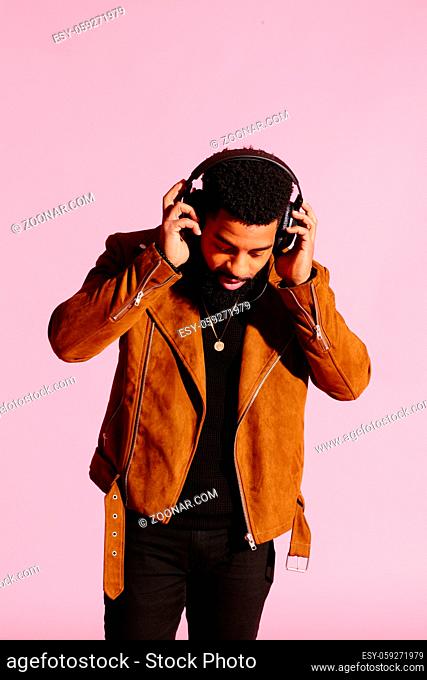 Stylish, handsome and cool African American man with beard, listening to music, isolated on pink studio background