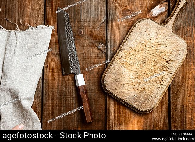metal kitchen knife and wooden cutting board on a table made of brown wooden boards, top view