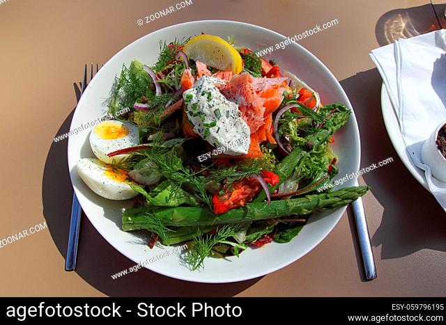 Salat mit Lachs, Ei und grünem Spargel auf einem weißen Teller. Fresh salad with salmon, egg and green asparagus on a white plate