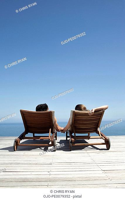 Couple laying in lounge chairs near ocean