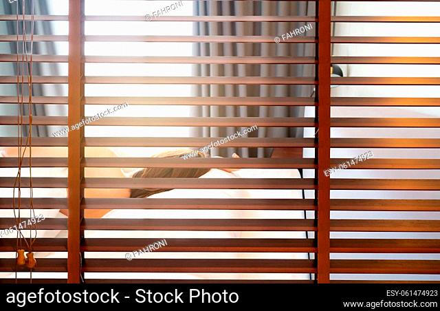 Wooden Venetian blinds. Blackout curtain between bathroom and bedroom in hotel with back view of woman sleep under white blanket on bed in the morning