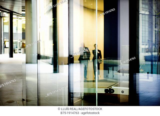 reflection of two executives walking through the lobby of an office building in City of London, England, UK