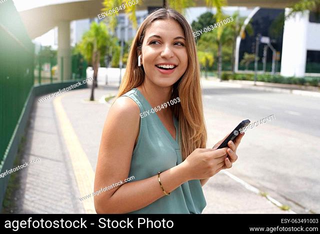 Beautiful Brazilian girl using wireless earphones to listening music in city street