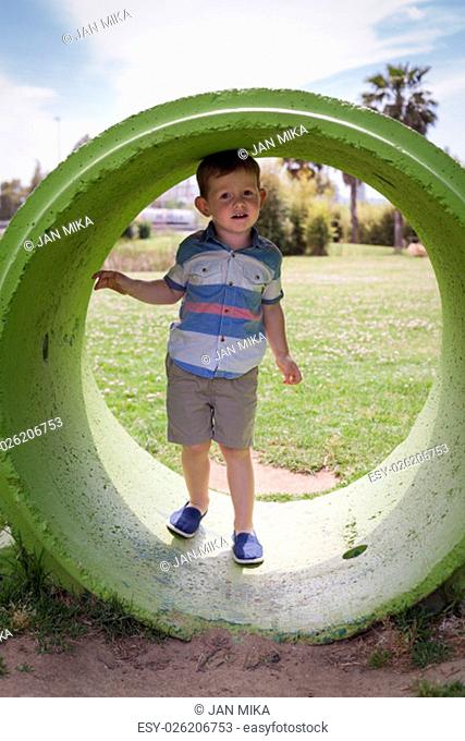 Portrait of a child boy hiding inside the concrete ring and playing in park during summer day