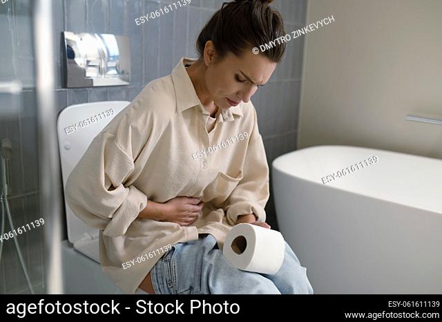 Indigestion. Young woman sitting on a toilet and suffering from indigestion