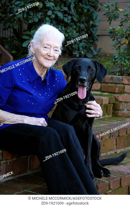 An old woman poses with her black lab best friend