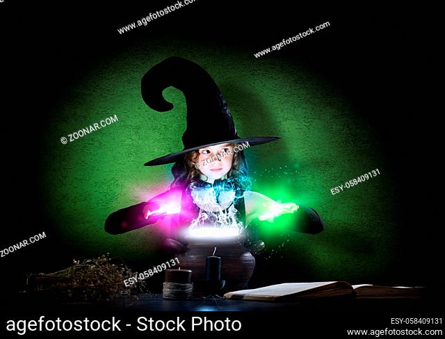 Little Halloween witch reading conjure from magic book above pot