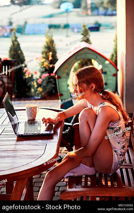 Woman working at home, using portable computer, sitting on patio on summer day. Candid people, real moments, authentic situations