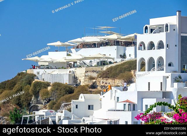 Summer Greece. Sunny day in Santorini caldera. Balconies, sun umbrellas and white houses in Oia