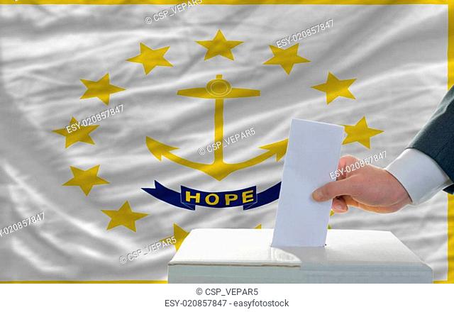 man putting ballot in a box during elections in front of flag american state of rhode island