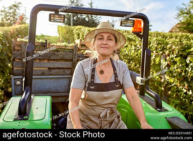 Mature farmer wearing straw hat on tractor in vineyard