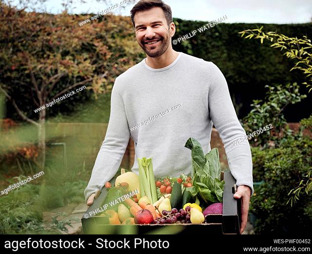 Happy man carrying a fresh vegetable box in garden