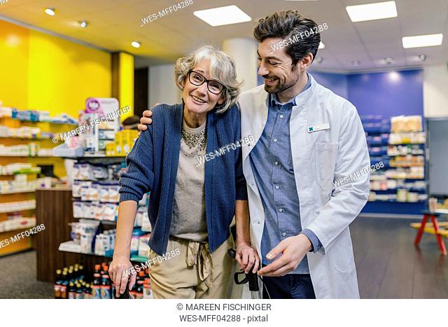 Portrait of smiling pharmacist and customer with wheeled walker in pharmacy