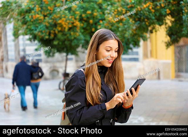 Portrait of a beautiful smiling woman using a mobile phone in city street with tangerine trees