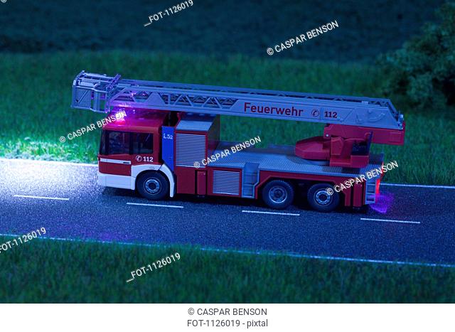 A diorama of a miniature toy fire truck driving on a road at night
